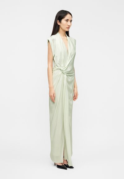 Robe longue vert clair en tissu soyeux avec un décolleté en V profond, une taille nouée et une fente. Elle présente des manches courtes et une silhouette fluide.