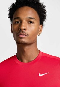 Rød sportslig skjorte med rund hals, laget av et glatt og tettsittende materiale. Har en hvit Nike-logo på brystet.