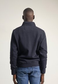 Chaqueta de pullover en color marino con un cuello alto, textura acanalada y mangas largas; combinada con unos jeans azules que tienen doble bolsillo trasero.