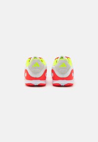 Des chaussures de sport rouges et blanches avec une tige en maille, des accents en jaune fluo et un collier rembourré. Elles sont dotées d'une semelle texturée pour l'adhérence et le soutien.