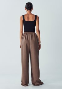 Bodycon senza maniche di colore nero abbinato a pantaloni della tuta marroni, larghi e con vita elastica, su uno sfondo chiaro.