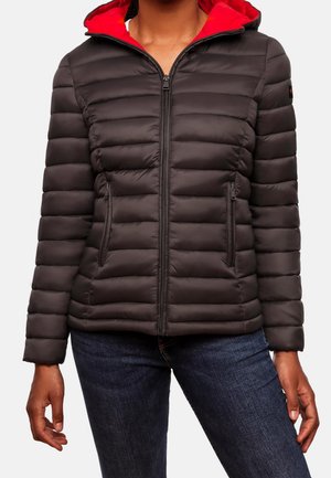 Vrouw draagt een zwart doorgestikt jack met een rood gevoerde capuchon, een rits aan de voorkant en ritszakken, gecombineerd met donkerblauwe jeans.