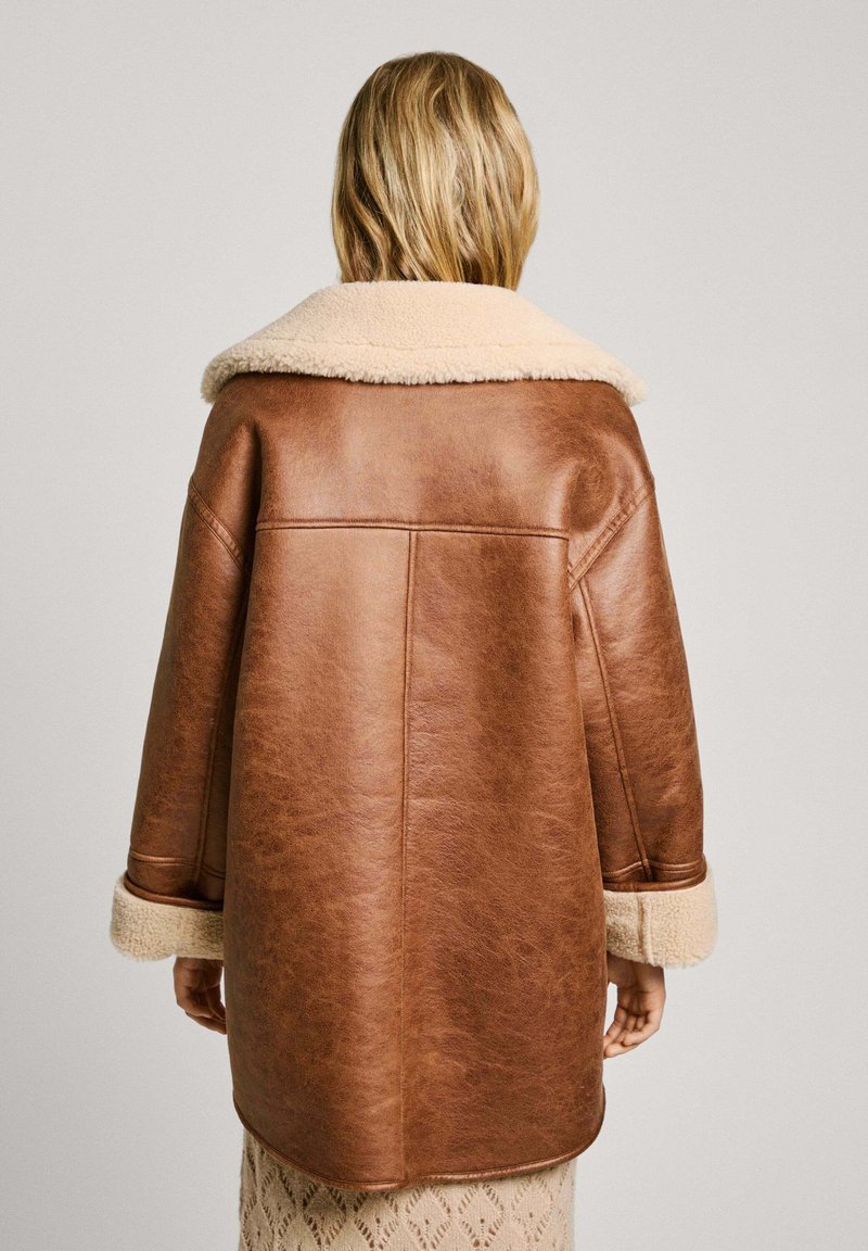 Veste en simili cuir marron avec un col et des poignets en sherpa beige. Surdimensionnée, avec une texture lisse et des détails de couture soignés.