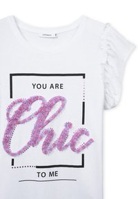 T-shirt bianco con maniche corte a volant, che presenta un grafiche testurizzata floreale rosa e viola con la scritta "Chic" all'interno di un riquadro nero, e testo nero sopra e sotto.