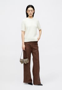 Un pull en maille écru à manches courtes associé à un pantalon large en simili cuir marron et un petit sac à main texturé avec des boucles.