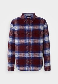 Veste-chemise à manches longues avec motif à carreaux bordeaux, bleu marine et blanc, avec deux poches poitrine à rabat avec boutons.