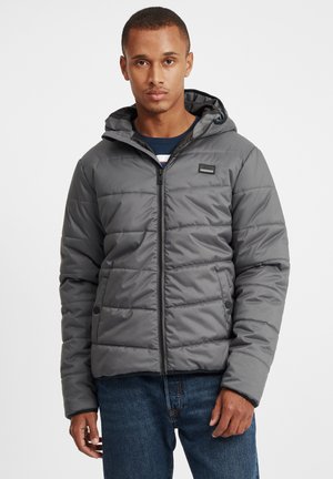 Graue Steppjacke mit Kapuze, ausgestattet mit einem Reißverschluss vorne, horizontalem Steppmuster und seitlichen Taschen. Darunter wird ein blau gestreiftes Hemd getragen.