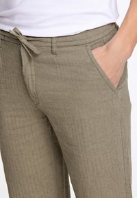 Beige Herringbone-Muster Hose mit Gummizugbund und Seitentaschen, aus einem strukturierten Stoff gefertigt.