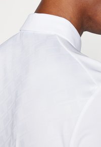 Hvit polo skjorte med et subtilt geometrisk mønster, strukturert krage og glatt, noe blankt stoff.
