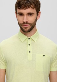 Koszulka polo w jasnym żółtym kolorze, z krótkim rękawem, kołnierzykiem, pięcioma guzikami z ciemnymi guzikami oraz kieszonką na piersi z pasującym detalem guzika.