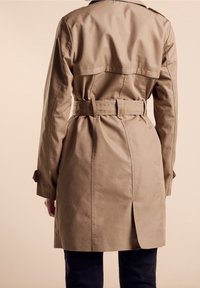 Kaki trenčkot s páskem v pase, zadním rozparkem a bočními kapsami. Vyroben z hladké látky s klasickým límcem a na míru střiženým střihem.