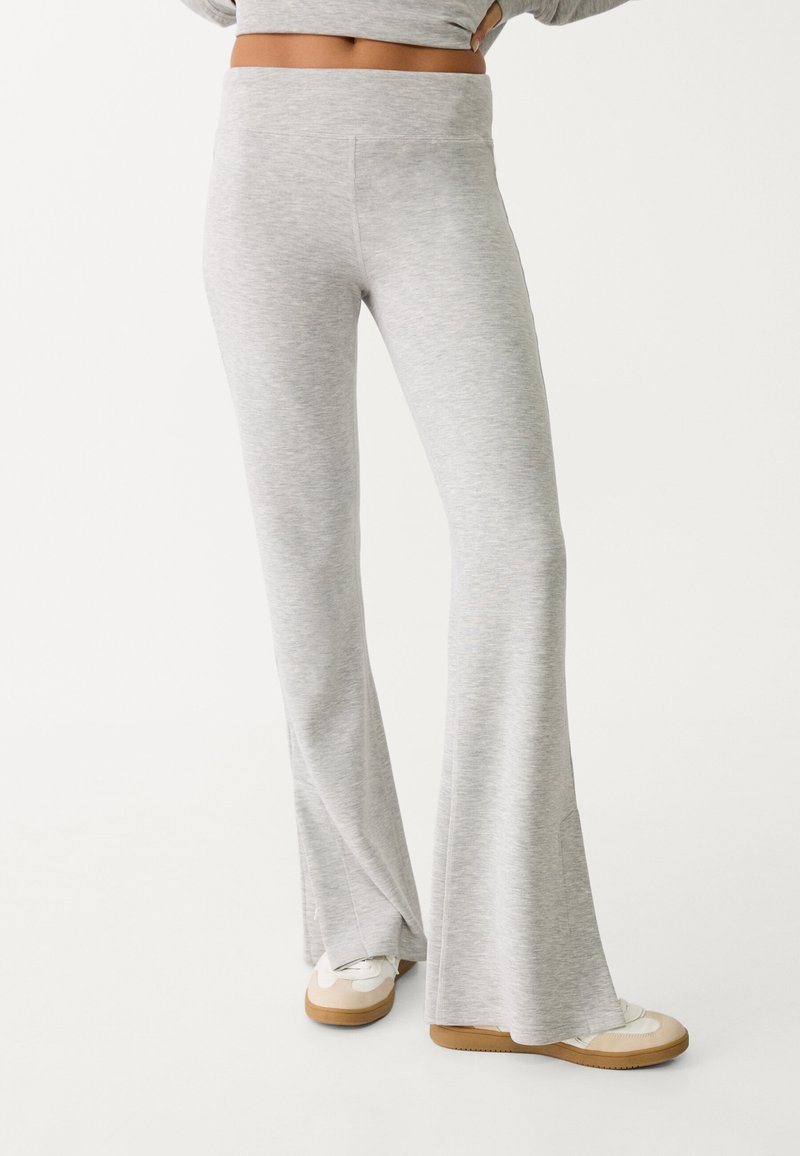 Šedé rozšířené tepláky s hladkým povrchem a širokým pasem. Obsahují švy na zadní straně a jsou kombinovány s bílými teniskami.