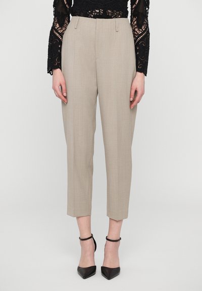 Pantalons beiges ajustés avec une coupe droite et une longueur légèrement raccourcie. Dispose d'une texture lisse et de deux poches frontales, associés à des talons noirs.