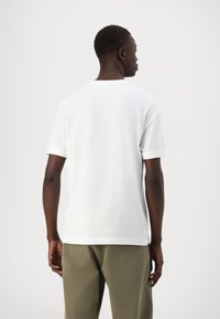 Witte katoenen t-shirt met korte mouwen, een losse pasvorm en ronde hals, weergegeven vanuit de achterkant, gecombineerd met olijfgroene broeken.