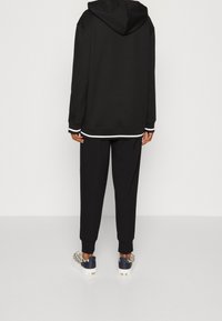Sudadera con capucha negra con detalles en blanco, combinada con pantalones jogger negros. Zapatillas texturizadas destacadas con un diseño estampado y acentos en azul marino.