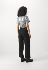 Haut court manches courtes argenté brillant associé à un pantalon noir ample à texture, avec une ceinture à boucle et des bottes noires épaisses.