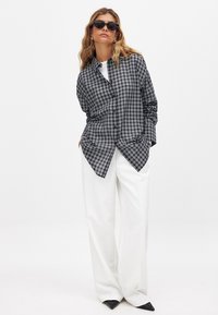 Button-up shirt in black and white check pattern, long sleeves, relaxed fit. Paired with white wide-leg trousers and black pointed shoes.