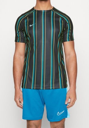 Mand iført sort sportstrøje med gule og blågrønne vertikale striber og blå sportsshorts med hvide Nike-logoer, stående mod en hvid baggrund.