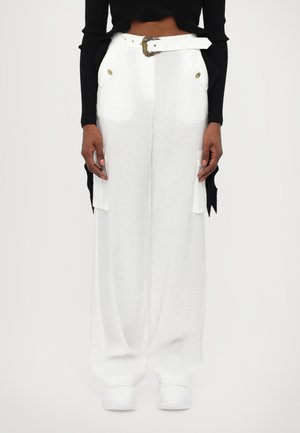White wide-leg trousers with a textured fabric, featuring prominent side pockets, a wide belt with an ornate buckle, and a loose fit.