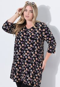 Schwarze Tunika mit V-Ausschnitt, die ein Muster aus verschiedenen kreisförmigen Formen in Beige, Lila und Grau aufweist. Dreiviertelärmel und lockere Passform.