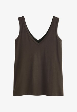 Femme portant un blazer bordeaux et un pantalon à jambes larges avec un haut noir à col en V, debout les mains dans les poches devant un fond beige et blanc.