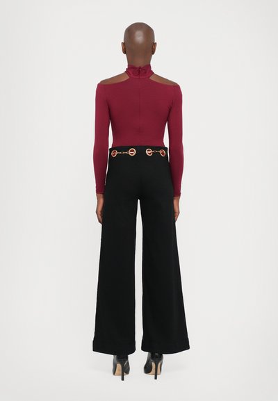 Bordeaux lange mouw bodysuit met een hoge kraag, gecombineerd met zwarte wijde broek met een gouden ronde kettingriem. Glad stoffen textuur.