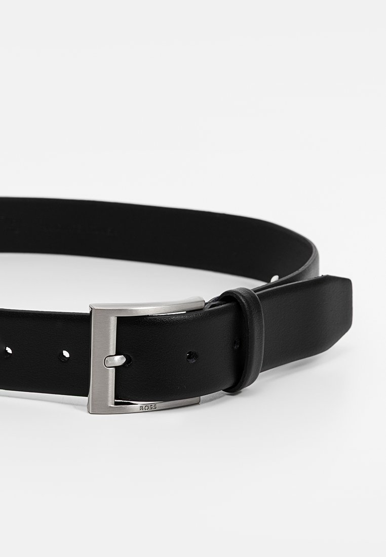 Ceinture en cuir noir avec une boucle en métal argenté. Elle dispose de plusieurs trous pour l'ajustement de taille. Texture lisse, design classique.