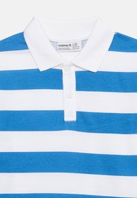 Λευκό και μπλε ριγέ πόλο πουκάμισο με λευκό γιακά και δύο λευκά κουμπιά στην πατιλέτα, ετικέτα μεγέθους ορατή μέσα στον γιακά.