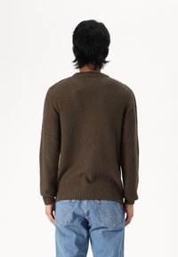 Suéter de punto marrón con un patrón texturizado, puños y dobladillo acanalados, combinado con jeans de mezclilla azul claro. Vista desde la parte posterior.