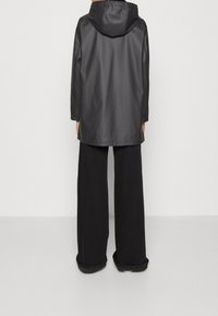 Zwarte waterdichte jas met een capuchon, lange mouwen en een ontspannen pasvorm. Gecombineerd met wijde zwarte broeken voor een gelaagde look.