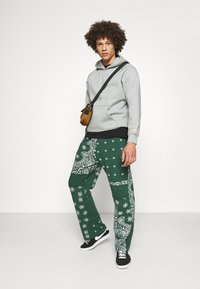 Sudadera gris con capucha, camiseta negra superpuesta, pantalones verdes con patrones de paisley blancos y zapatillas negras con suelas blancas.