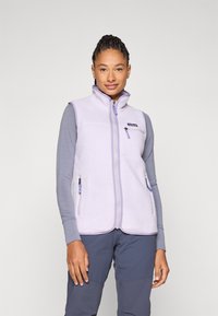 Gaiši violets fliša veste ar augstu apkakli, priekšējo zipsu un ar rāvējslēdzējiem slēgtām kabatām. Valkāta virs pelēka garām piedurknēm krekla, kuram ir maiga tekstūra.
