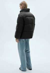 Sort dunjakke med højt krave og kviltet design. Sammen med lyseblå vide jeans og sorte sko.