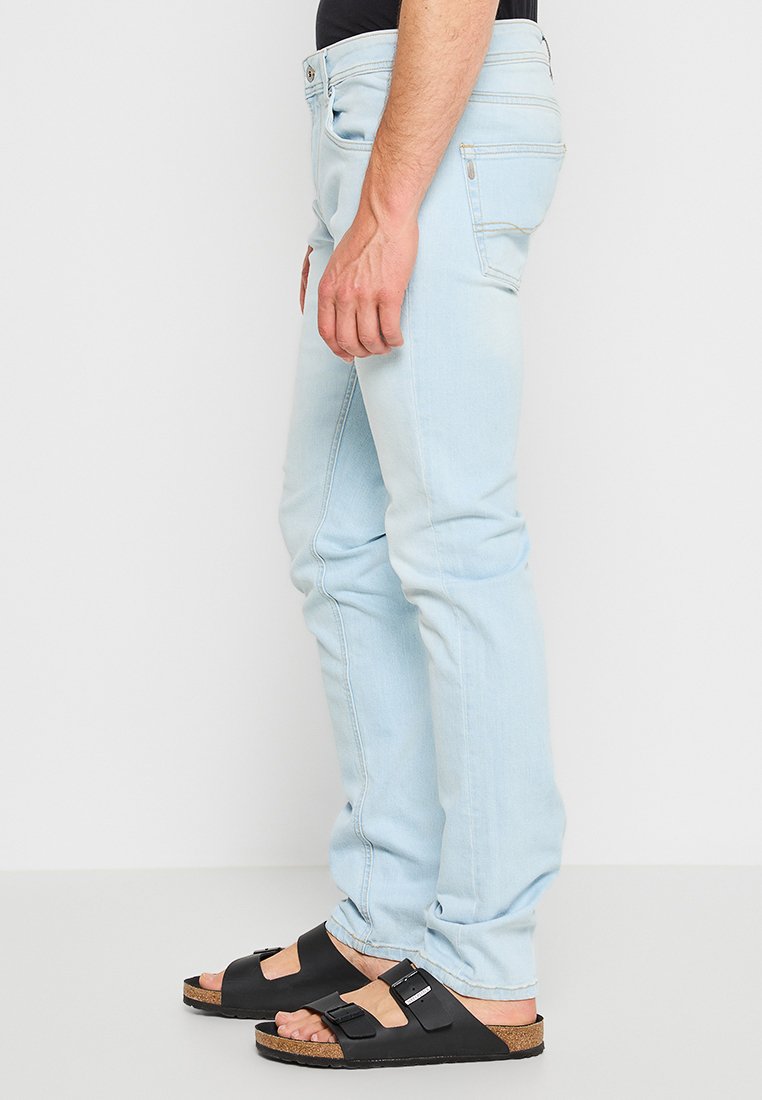 Helle blaue Denim-Jeans mit schmalem Schnitt und leichter Verblassung. Verfügt über fünf Taschen und Metallbeschläge. Kombiniert mit schwarzen Sandalen.