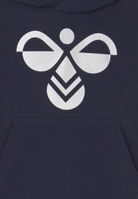 Marineblauwe hoodie met een grote witte grafische print die lijkt op een abstracte bij, met ronde en geometrische vormen en een centrale zak.