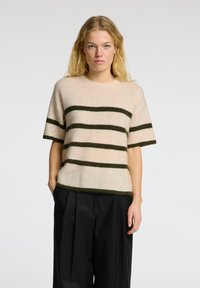 Lys beige sweater med mørkegrønne striber. Korte ærmer, rund halsudskæring, lavet af blødt materiale med en let løs pasform og rå kant.