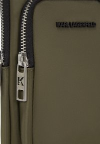Borsa da viaggio in nylon verde oliva con zip nera e finiture in argento, dotata di etichetta con logo e superficie liscia al tatto.