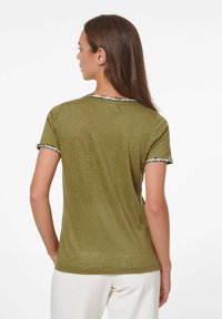 Olijfgroen t-shirt met korte mouwen, voorzien van zwart-witte decoratieve biezen op de kraag en de randjes van de mouwen. Zacht, lichtgewicht stof.