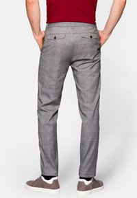 Szare spodnie w kratę o dopasowanym kroju, z dwoma tylnymi kieszeniami zapinanymi na guziki, noszone z białymi i szarymi sneakerami.