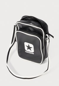 Borsa a tracolla in vinile nero con rifiniture bianche, dotata di due scomparti con zip e un grande logo con una stella sul davanti. Cinghia regolabile.