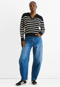 Black and white striped knit pullover with a V-neck and collar, paired with loose blue denim jeans and black sneakers with white stripes.