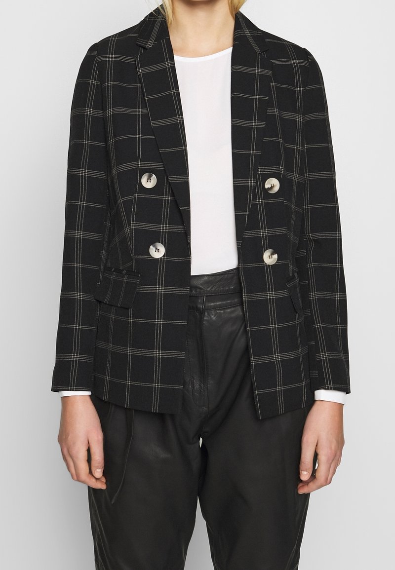 Två-knapprad svart kavaj med vit rutmönster, med silverbiseringar och spetsiga slag. Matchad med en vit topp och läderbyxor.