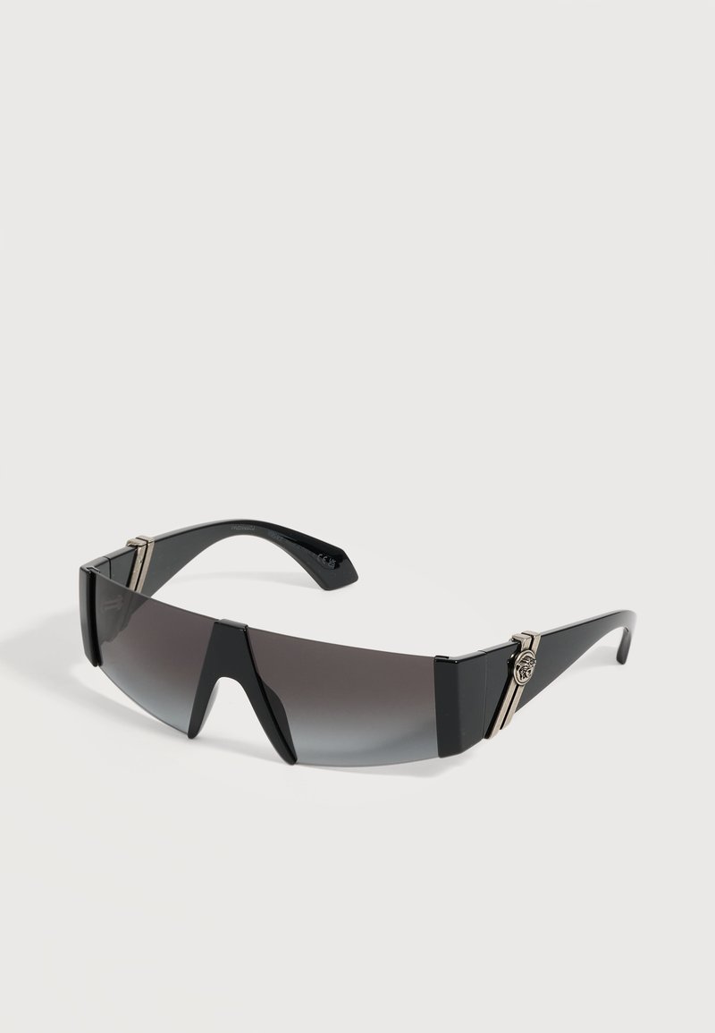 Lunettes de soleil enveloppantes noires avec verres dégradés foncés et accents argentés décoratifs sur les branches sur un fond uni.