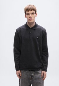 Σκούρο γκρι πόλο μπλουζάκι με μακριά μανίκια και γιακά. Διαθέτει λογότυπο στο στήθος και κουμπωτό άνοιγμα. Υφασμάτινη υφή με ριμπ μανσέτες.