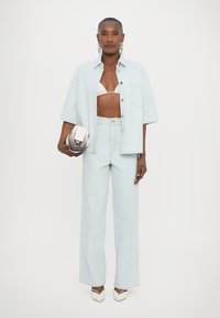 Conjunto de denim azul claro, incluindo uma camisa cropped com botões e calças largas, complementado com um top de bikini branco e uma pequena bolsa branca.