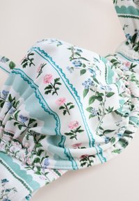 Cupa de sutien din material alb cu margini adunate, prezentând un model floral cu dungi verzi și flori roz și albastre.