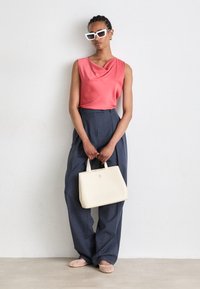 Ταιριαστό κορal σατέν τοπ, ψηλόμεσες ναυτικές παντελόνες, κρέμ τσάντα με λογότυπο �και ροζ παπούτσια slip-on. Γυαλιά ηλίου με διάφανο σκελετό.