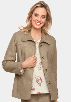 Beige Wollmischung Jacke mit Kragen, vier Knöpfen und Seitentaschen, getragen über einem weißen Pullover mit rosa Blumenmustern.