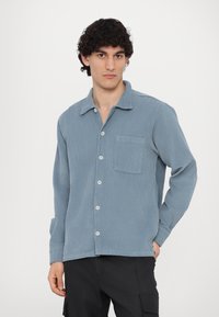 Light blue corduroy shirt with a point collar, long sleeves, and a chest pocket. Features button closure and ribbed texture.