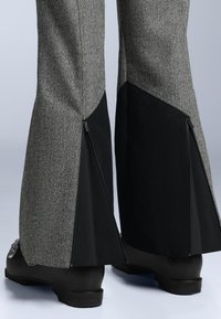 Szürke halszálkás nadrág fekete oldalsó panelekkel, cipzárakkal a szár végén. Simább textúrájú, szabott fazonú, lapos derékrésszel.